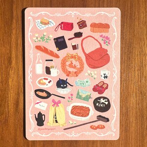 Pu&ograve; includere: Una carta rosa illustrata con un bordo decorativo, raffigurante vari oggetti, tra cui cibo, una borsa rossa, un gatto nero e una ghirlanda. La carta include il testo "@jennifergangart".