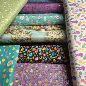 May include: A stack of fabric featuring various Easter-themed patterns, including bunnies, eggs, and flowers. The fabrics are in a variety of colors, including green, blue, purple, and white.