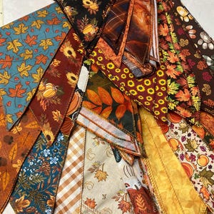 May include: A collection of fabric scraps in various autumnal colors and patterns, including leaves, pumpkins, and plaid. The fabric scraps are arranged in a triangular shape, with the points of the triangles facing outwards.