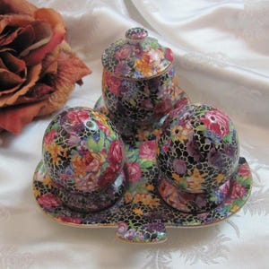 Könnte beinhalten: Ein Set aus drei vintage Salz- und Pfefferstreuern mit Blumenmuster. Die Streuer sind schwarz mit einem weißen Blumenmuster und stehen auf einem passenden Tablett.