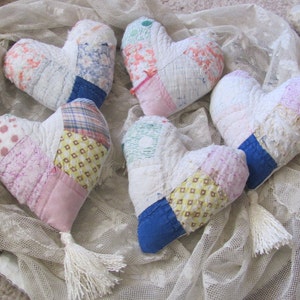 May include: Five handmade patchwork heart-shaped pillows with white, pink, blue, and yellow fabric. Each pillow has a white tassel.