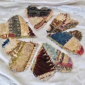 Puede incluir: Colección de siete parches de tela en forma de corazón en varios colores y texturas. Los parches están hechos de una mezcla de materiales, incluyendo terciopelo y lino, y están cosidos con hilo de contraste. Los corazones están dispuestos en un patrón circular.