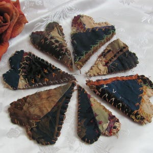 Puede incluir: Una colección de ocho corazones de tela patchwork en varios tonos de marrón, azul y crema. Los corazones están cosidos juntos con costuras visibles y tienen una estética rústica y vintage.