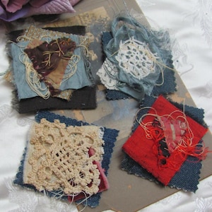 May include: Four fabric squares featuring a variety of textures and colours, including blue, red, brown, and white. Each square is layered with different fabrics and lace, creating a unique and textured appearance.