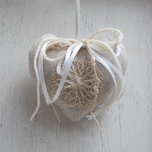 May include: A beige heart-shaped cushion with white lace and white ribbon accents.