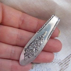 May include: A silver-toned, ornate, floral-patterned, spoon-shaped, metal money clip.