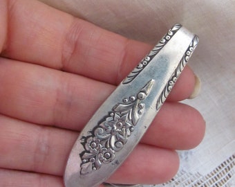 May include: A silver-toned, ornate, floral-patterned, spoon-shaped, metal money clip.