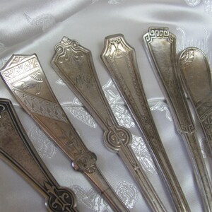 May include: Six silver spoons with ornate handles. The spoons have different designs and patterns.