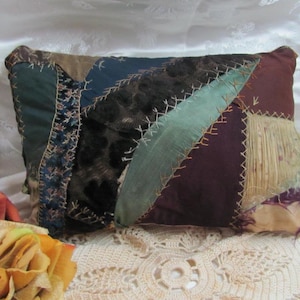 May include: A rectangular patchwork pillow with a variety of fabrics in shades of green, blue, brown, and purple. The pillow is hand-stitched with visible thread and has a vintage aesthetic. A decorative rose and a yellow rose are in the foreground.