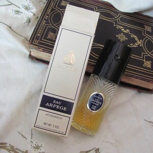 May include: A vintage bottle of Lanvin Eau Arpege perfume with its original box. The box is white with black text and a gold emblem. The perfume bottle is clear with a black cap and a label that reads "Eau Arpege". The net weight is 2 oz.
