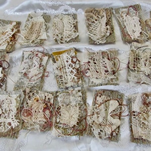 May include: A collection of small, rectangular fabric pieces with intricate lace and thread details. The pieces feature a mix of beige, cream, and brown tones, with visible textures and patterns. The arrangement suggests a craft or textile art project.