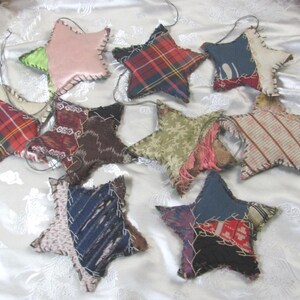 May include: A collection of ten star-shaped fabric ornaments featuring various patterns including plaid, stripes, and solid colours. Each star is constructed from multiple fabric patches joined with visible whipstitching and includes a thin wire loop for hanging.