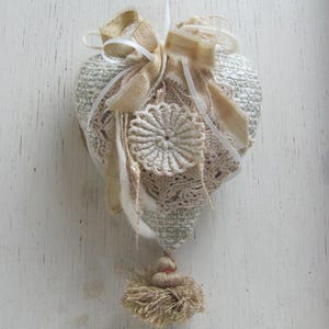 May include: A white heart-shaped pillow with crocheted lace and a gold tassel. The pillow is decorated with a white ribbon and a gold bow.