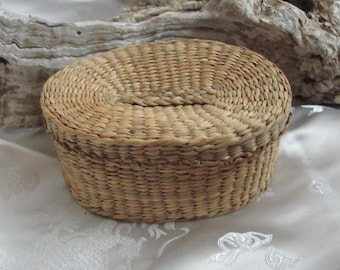 May include: A round, woven basket made of natural materials. The basket has a lid and is made with a tight weave.