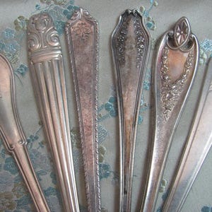 May include: Six silver spoons with ornate designs. The spoons have different patterns and styles, including a floral design, a geometric design, and a simple design.