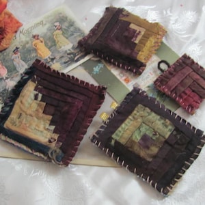 May include: Four handmade fabric squares with a log cabin quilt pattern. The squares are in shades of brown, purple, and green. The fabric is stitched together with a contrasting thread.
