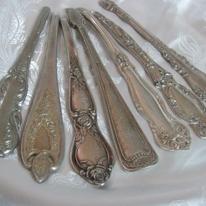 May include: A set of seven antique silver-plated serving spoons with ornate floral designs. The spoons have a long, slender handle and a rounded bowl.