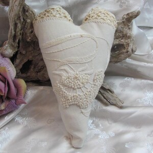 May include: A white heart-shaped pillow with delicate lace trim and intricate embroidery. The pillow is made of a soft, textured fabric and has a vintage aesthetic.