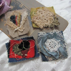 May include: Four handmade fabric squares featuring different textures and colours. Each square has a unique design with lace, embroidery, and fabric scraps. The squares are ideal for crafting or decorating.