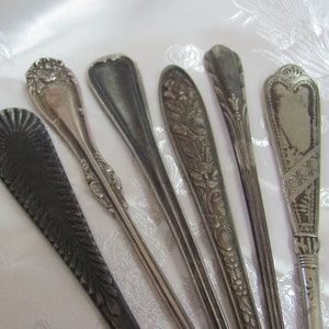 May include: Six silver-plated, ornate, decorative spoons with various designs. The spoons have a long, slender handle and a rounded, spoon-shaped bowl.