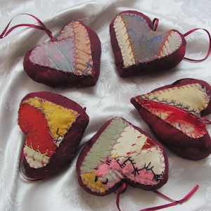 以下が含まれることがあります： 異なるパッチワークのデザインが施された、赤いフェルト製のハート型のオーナメントが5つ。各ハートには吊り下げ用のループが付いています。