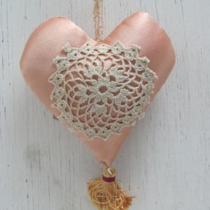 May include: A peach-coloured heart-shaped cushion with a white crocheted doily and a gold tassel.