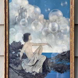 May include: A framed print featuring a seated figure gazing upwards towards large bubbles floating in a blue sky. The artwork includes a castle, trees, and water, all within a gold-colored frame.