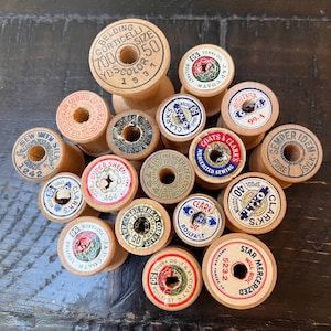 May include: A collection of vintage wooden spools with colorful labels. The spools vary in size and feature text such as "Belding Corticelli," "Clark's," and "Star Mercerized." The labels display various colors and designs, adding to the antique aesthetic.