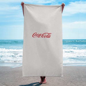 May include: A white beach towel with the red Coca-Cola logo printed on it.