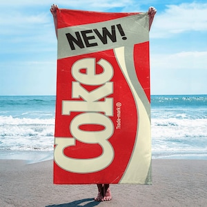 May include: A red beach towel with the words "NEW!" and "Coke" in white lettering. The word "Coke" is in a large, stylized font and the word "Trade-mark" is in smaller lettering below it.