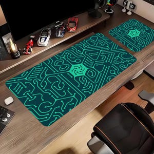 May include: A teal and green computer desk mat and matching mousepad with a circuit board design. The rectangular mat is long and thin, with a square mousepad to the side. The design has a central starburst pattern.