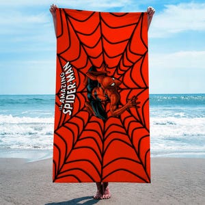 May include: A red beach towel with a black spider web design and a cartoon image of Spider-Man in the center. The text "The Amazing Spider-Man" is printed on the towel.