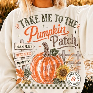 Pode incluir: Uma camisola de gola redonda cor de creme com uma impress&atilde;o gr&aacute;fica com o texto "TAKE ME TO THE PUMPKIN PATCH". O design inclui uma ab&oacute;bora laranja grande, uma placa de madeira, um girassol, folhas de outono e um selo circular.
