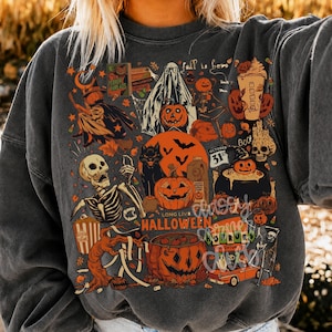 May include: A charcoal gray crewneck sweatshirt featuring a vibrant collage of Halloween-themed illustrations including a skeleton, a ghost, pumpkins, a black cat, a witch, a cauldron, and the text "Fall is here" and "Long Live Halloween".