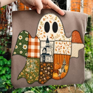 May include: A brown t-shirt featuring a large ghost-shaped appliqué made of various fabric patches. The patches display patterns of autumn leaves, orange gingham, a haunted house illustration, pumpkins, and floral designs with black stitching.