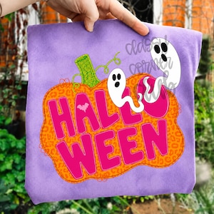 Puede incluir: Una camiseta de color morado claro con un gr&aacute;fico de una gran calabaza naranja con estampado de leopardo. La calabaza contiene el texto rosa brillante HALLOWEEN y un peque&ntilde;o murci&eacute;lago blanco. Dos fantasmas blancos flotan encima.