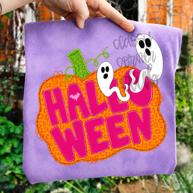 Puede incluir: Una camiseta de color morado claro con un gr&aacute;fico de una gran calabaza naranja con estampado de leopardo. La calabaza contiene el texto rosa brillante HALLOWEEN y un peque&ntilde;o murci&eacute;lago blanco. Dos fantasmas blancos flotan encima.