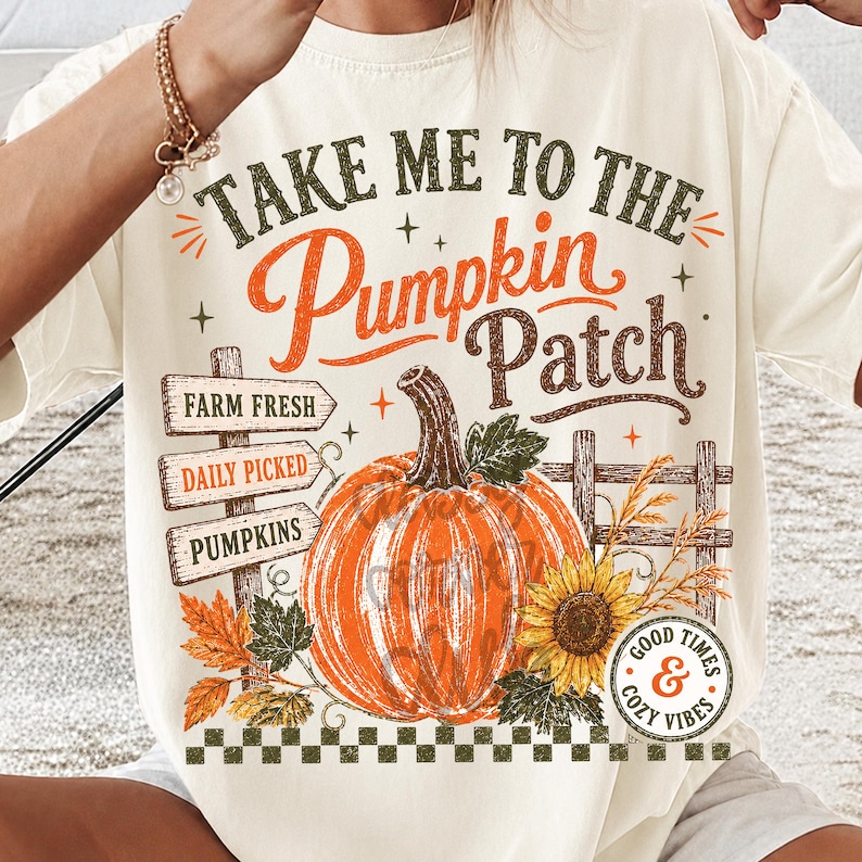 Pode incluir: Uma t-shirt de cor creme com um gr&aacute;fico que inclui o texto "TAKE ME TO THE PUMPKIN PATCH". O design apresenta uma ab&oacute;bora laranja grande, um girassol, folhas de outono, uma placa de madeira com "FARM FRESH", "DAILY PICKED", "PUMPKINS" e uma cerca.