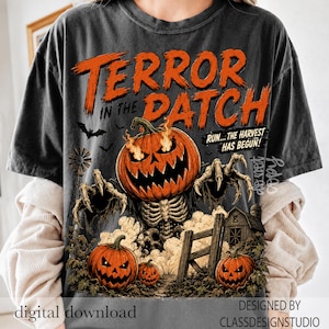 Puede incluir: Una camiseta gris carb&oacute;n con un gr&aacute;fico de una criatura calabaza en llamas con manos esquel&eacute;ticas. El texto dice TERROR IN THE DATCH y RUN... THE HARVEST HAS BEGUN! Otros elementos incluyen un molino de viento, una valla de madera y calabazas.