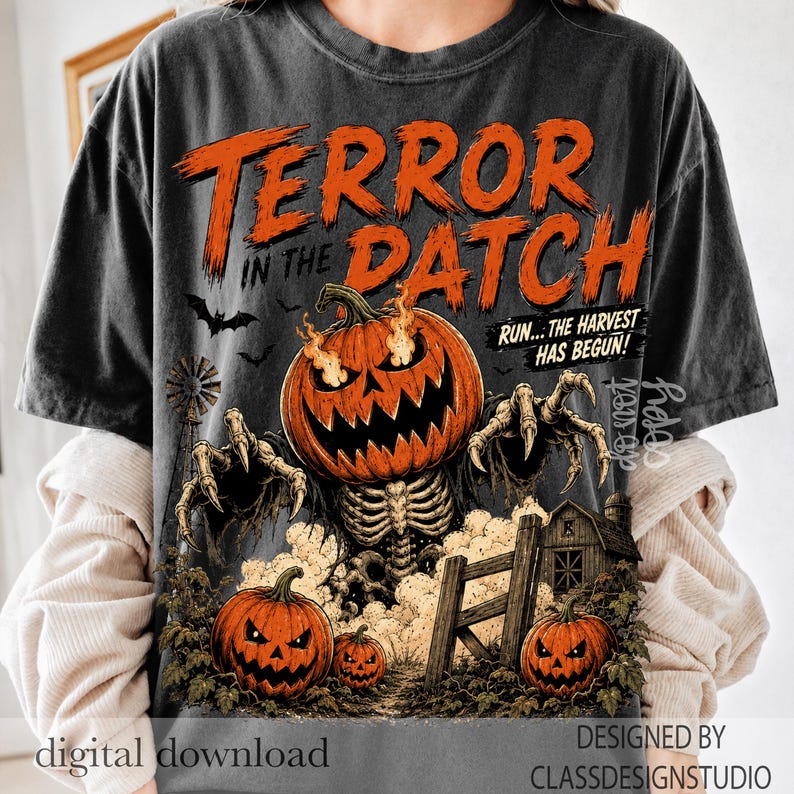 Puede incluir: Una camiseta gris carb&oacute;n con un gr&aacute;fico de una criatura calabaza en llamas con manos esquel&eacute;ticas. El texto dice TERROR IN THE DATCH y RUN... THE HARVEST HAS BEGUN! Otros elementos incluyen un molino de viento, una valla de madera y calabazas.