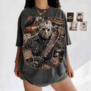 May include: A charcoal gray oversized t-shirt featuring a graphic print of a hockey mask-wearing figure holding a machete. The design includes a raven, a pumpkin, skulls, and text reading Camp Crystal Lake, No Swimming After Dark, and October 31.