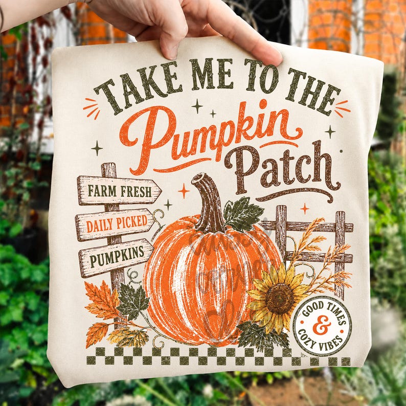 Pode incluir: Uma t-shirt de cor creme com uma impress&atilde;o gr&aacute;fica com o texto "TAKE ME TO THE Pumpkin Patch". O design inclui uma ab&oacute;bora laranja grande, uma placa de madeira com "FARM FRESH", "DAILY PICKED" e "PUMPKINS", um girassol e v&aacute;rias folhas.