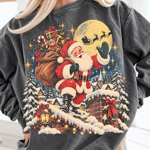 May include: A charcoal gray crewneck sweatshirt featuring a graphic of Santa Claus on a snowy rooftop with a sack of gifts, a brick chimney, pine trees, and a silhouette of a sleigh flying across a large yellow moon in the night sky.