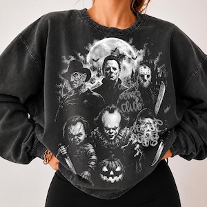 May include: A charcoal grey acid-wash crewneck sweatshirt featuring a large black and white graphic print of five iconic horror movie characters, a full moon, and a pumpkin. The text "spooky corner club" is printed in a cursive script overlay.