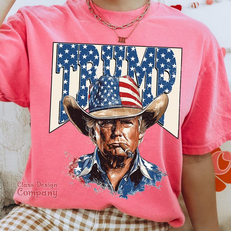 May include: Pink t-shirt with a graphic of a man wearing a cowboy hat with an American flag design. The text "TRUMP" is printed in white letters with stars around it.