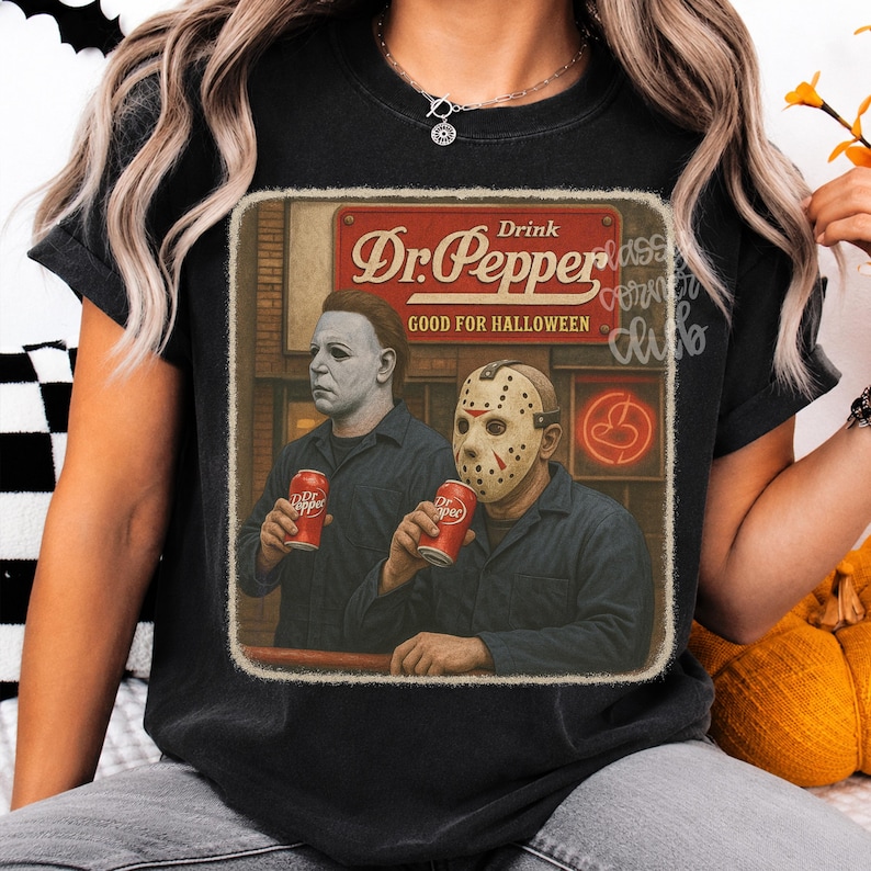 May include: A black t-shirt featuring a graphic print of two horror movie characters holding red soda cans. The text reads Drink Dr. Pepper GOOD FOR HALLOWEEN. The design has a vintage, distressed look with a rectangular border and muted colors.