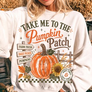 Pode incluir: Uma camisola branca de gola redonda com uma impress&atilde;o gr&aacute;fica com o texto "TAKE ME TO THE Pumpkin Patch". O design inclui uma ab&oacute;bora laranja grande, um girassol, uma placa de madeira com "FARM FRESH", "DAILY PICKED", "PUMPKINS" e uma cerca.