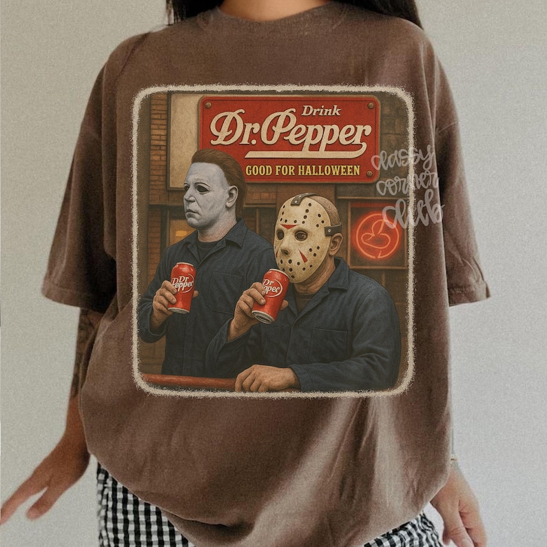 May include: A brown t-shirt featuring a graphic print of two horror movie characters wearing masks and dark shirts, each holding a red Dr. Pepper can. The graphic includes a red sign with the text Drink Dr. Pepper GOOD FOR HALLOWEEN.