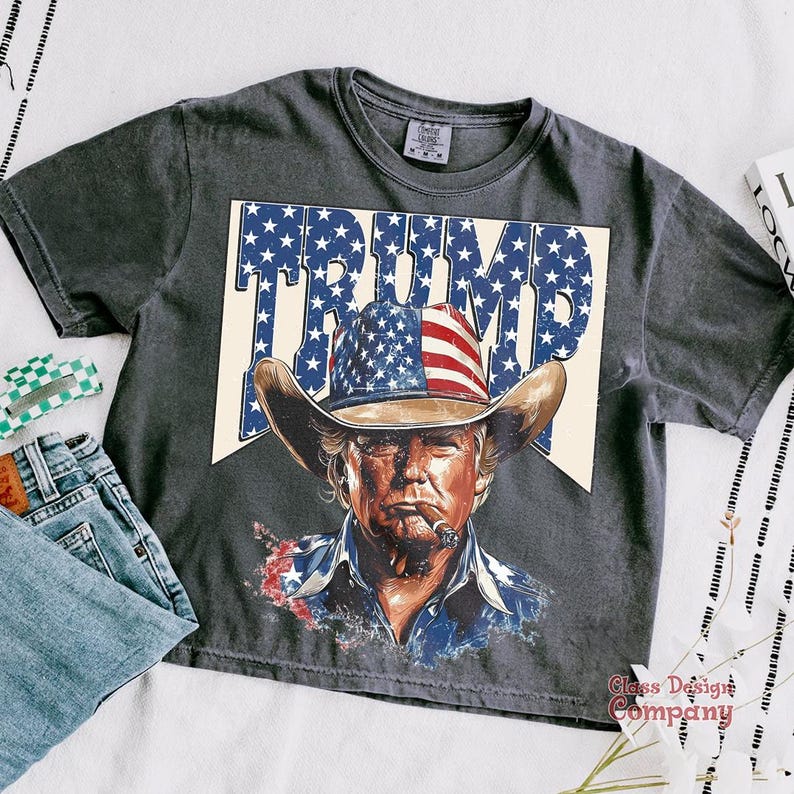 May include: A gray t-shirt with a vintage-style graphic of a man wearing a cowboy hat and a red, white, and blue bandana. The graphic says "TRUMP" in large letters.