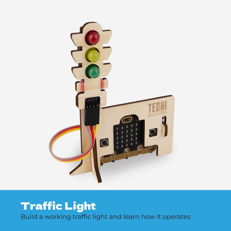Pode incluir: Um modelo de sem&aacute;foro de madeira com luzes circulares transl&uacute;cidas nas cores vermelha, amarela e verde. A estrutura inclui uma base com o texto TECHI EDUCATION e uma placa de microcontrolador com bot&otilde;es, conectada por um cabo plano colorido.
